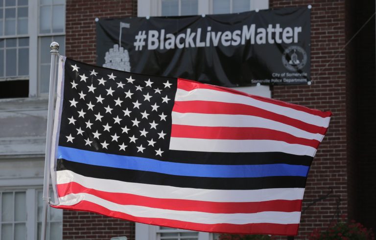 A United States flag, with blue and black stripes in support of law enforcement officers, flies at a protest by police and their supporters outside Somerville City Hall, Thursday, July 28, 2016, in Somerville, Mass.