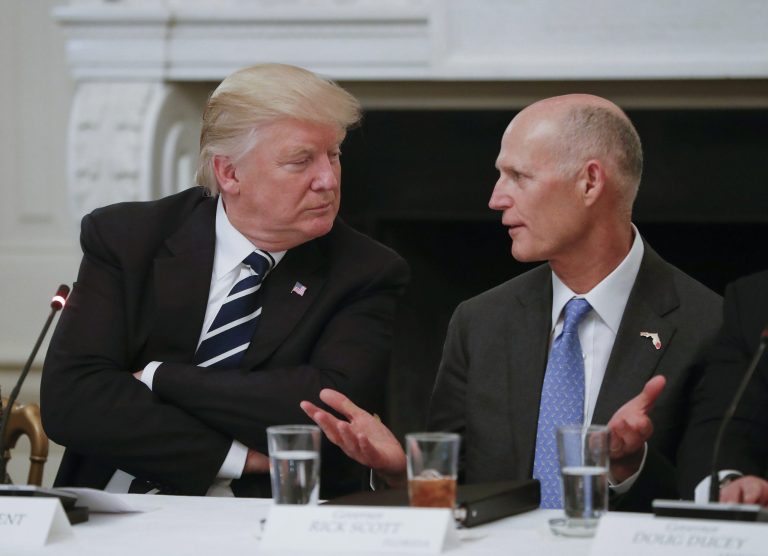 Then-President Donald Trump listens to then-Florida Gov. Rick Scott.