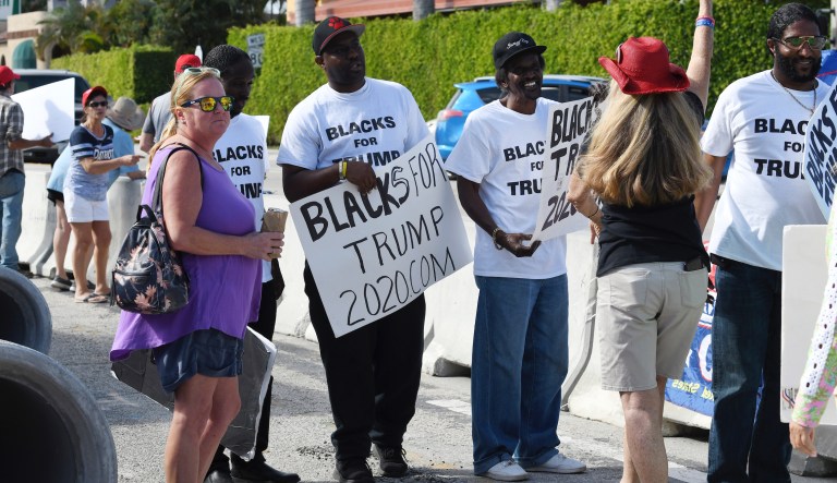 People, some holding "Blacks for Trump" signs, gather along Southern Boulevard as President Donald Trump's motorcade returns to Mar-a-Lago from the Trump International Golf Club located in West Palm Beach, Saturday, Jan. 18.