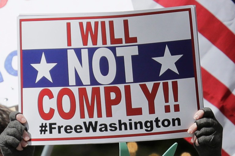 A person dressed as the statue of Liberty holds a sign that reads 