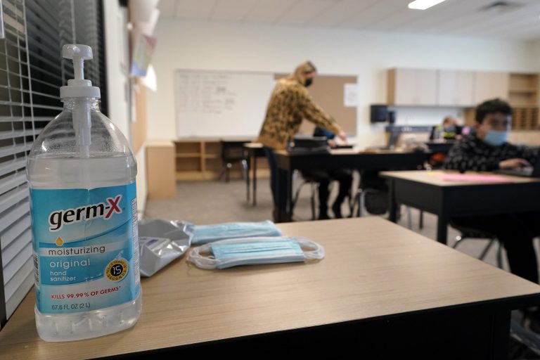 Hand sanitizer, wipes, and surgical masks rest on a desk in a fourth-grade classroom, Tuesday, Feb. 2, 2021, at Elk Ridge Elementary School in Buckley, Wash. The school has had some students in classrooms for in-person learning since September of 2020, but other students who attend the school are still learning remotely.