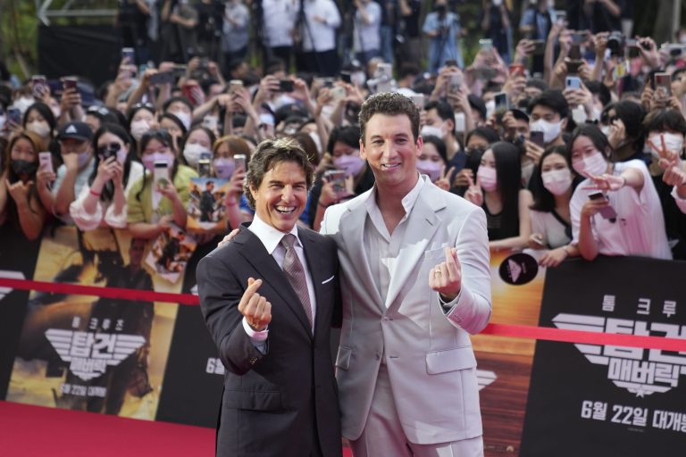 Tom Cruise, left, and Miles Teller gesture for photographers.