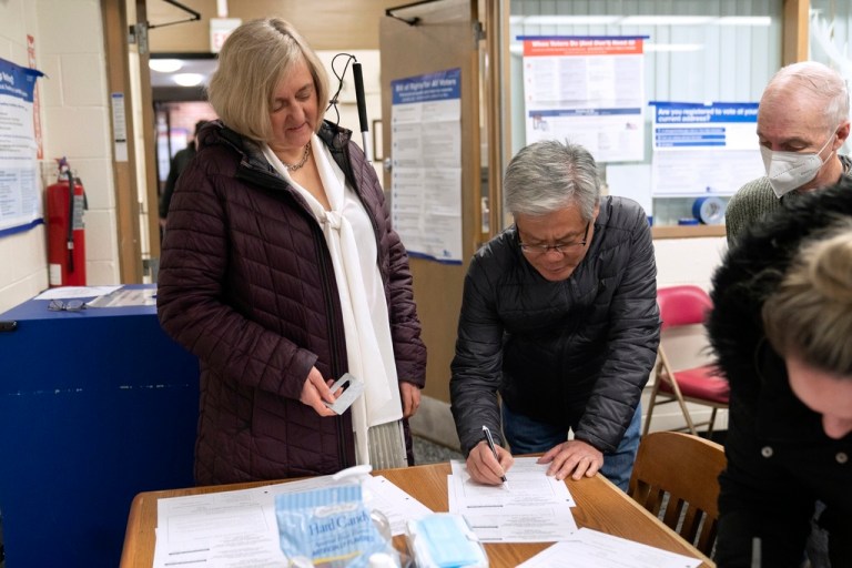 Patti Chang, left, who is blind, receives help from her husband Francisco Chang, center, and poll worker Bruce Mocking.