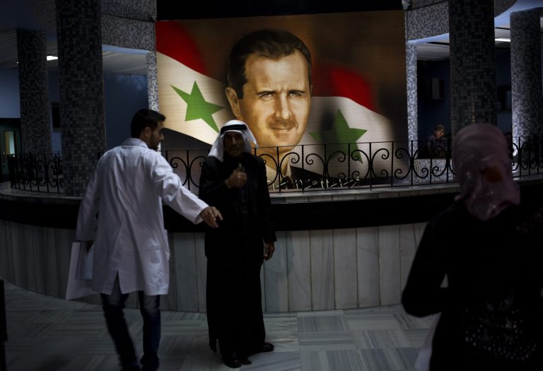 People walk through the Damascus General Hospital past a portrait of the President Bashar Assad in Damascus, Syria, Sunday, May 4, 2014. An official with Syria's Supreme constitutional Court said Assad and two others will be candidates in coming June presidential elections. (AP Photo/Dusan Vranic)