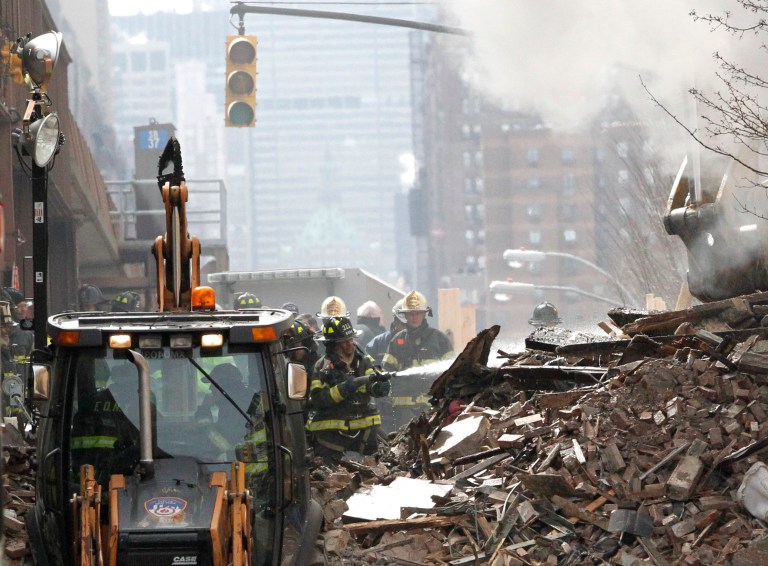 A firefighter applies water to rubble a day after a gas leak-triggered explosion, Thursday, March 13, 2014, in East Harlem, New York. Rescuers working amid gusty winds, cold temperatures and billowing smoke pulled additional bodies Thursday from the rubble of two apartment buildings that collapsed Wednesday. (AP Photo/Julio Cortez)