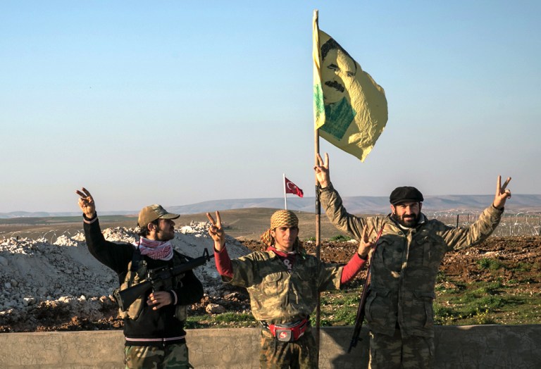 Syrian Kurdish militia members make a V-sign next to a poster of Abdullah Ocalan, jailed Kurdish rebel leader, and a Turkish army tank in Aleppo province, Syria. (AP Photo)