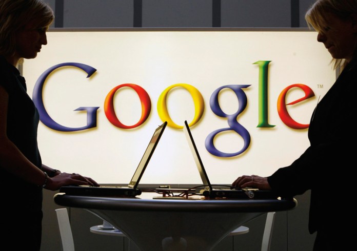 Exhibitors work on laptop computers in front of an illuminated Google logo.