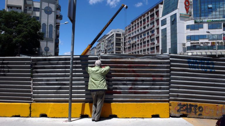 A man looks at a construction site from a small aperture from behind a sheet of metal fencing, in northern Greek city of Thessaloniki on Monday, June 2, 2014. Greece's trade federation said Monday that some 31 percent of all shops in the city center remain unoccupied as a result of the country's acute financial crisis that has seen unemployment hit record-high levels amid a six-year recession. The federation said the number of closed shops was slightly down compared to its last survey about six months ago. (AP Photo/Nikolas Giakoumidis)