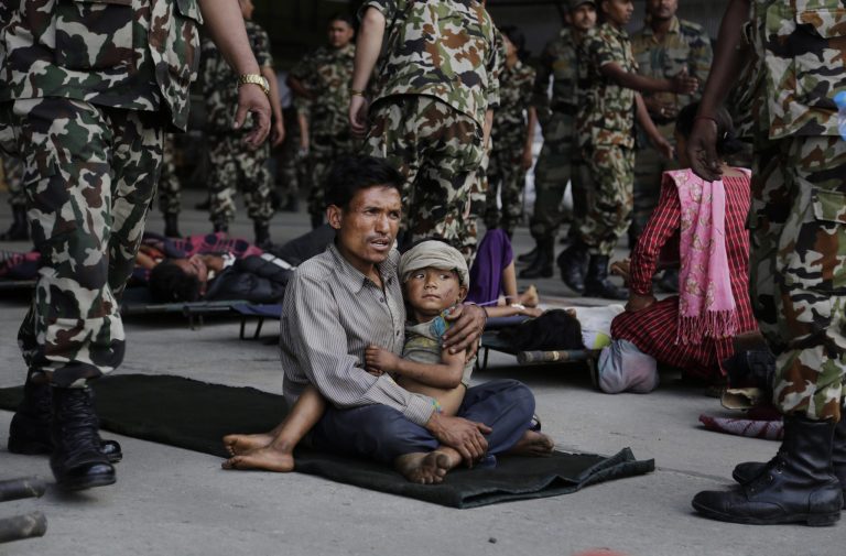 A man sits with a child on his lap as victims of Saturday's earthquake, wait for ambulances after being evacuated at the airport in Kathmandu, Nepal, Monday, April 27, 2015. The death toll from Nepal's earthquake is expected to rise depended largely on the condition of vulnerable mountain villages that rescue workers were still struggling to reach two days after the disaster. (AP Photo/Altaf Qadri)