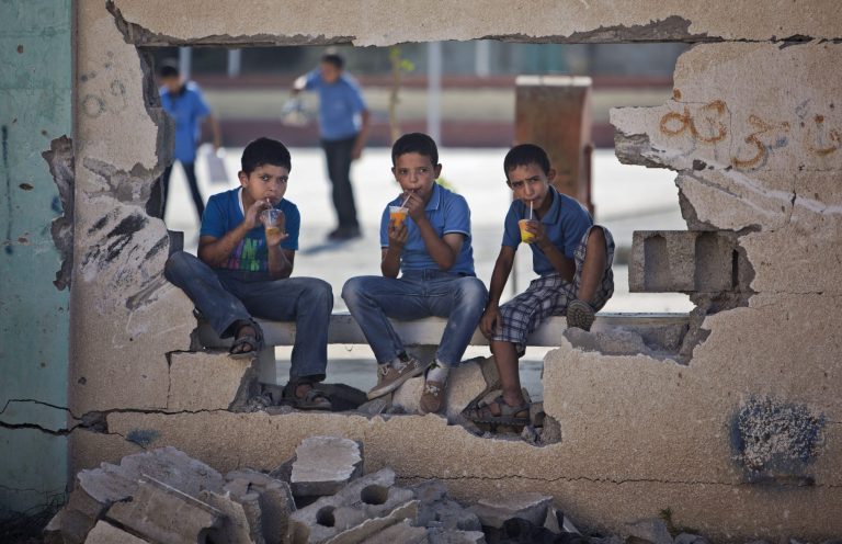 Palestinian school boys drink iced juice as they sit on a damaged wall of a school in Gaza City's Shijaiyah neighborhood, Sunday, Sept. 14, 2014. Some half million Gaza children made a delayed return to school on Sunday after a devastating 50-day war with Israel that killed more than 2,100 Palestinians and damaged hundreds of school buildings. (AP Photo/Khalil Hamra)