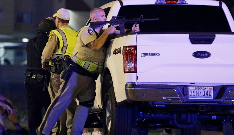 A police officer takes cover behind a truck at the scene of a shooting near the Mandalay Bay resort and casino on the Las Vegas Strip. Multiple victims were being transported to hospitals after a shooting late Sunday at a music festival in Las Vegas. (AP Photo/John Locher)