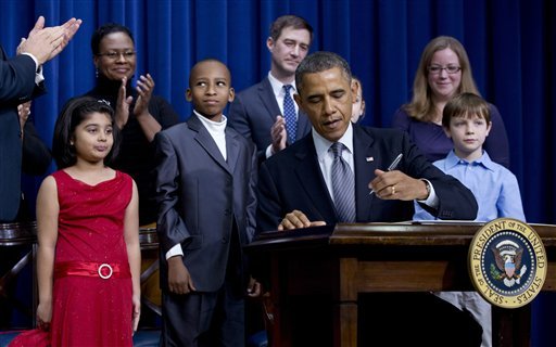 President Barack Obama, accompanied by Vice President Joe Biden, standing left clapping, and children who wrote the president about gun violence following last month's shooting at an elementary school in Newtown, Conn., signs executive orders to reduce gun violence, Wednesday, Jan. 16, 2013, in the South Court Auditorium at the White House in Washington. From left are: Biden Hinna Zeejah, 8, and Nadia Zeejah, Hinna's mother, Taejah Goode, 10, and Kimberly Graves, Taejah's mother, Julia Stokes, 11, and Dr. Theophil Stokes, Julia's father, Grant Fritz, 8, and Elisabeth Carlin, Grant's mother. (AP Photo/Carolyn Kaster)