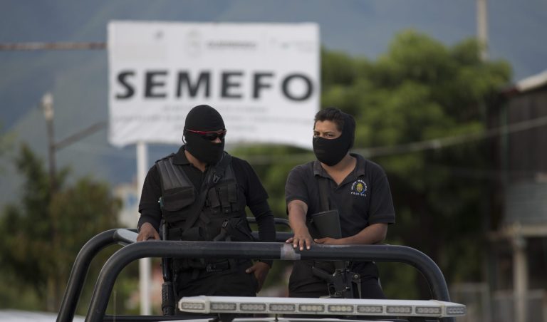 Masked police officers stand guard atop a vehicle oudside of the morgue in Iguala Mexico, Sunday Oct. 5, 2014. Relatives are demanding answers after security forces investigating the role of municipal police in clashes a week ago found a mass grave, raising fears the pits might hold the bodies of 43 students missing since last week in the violence that also resulted in six shooting deaths. (AP Photo/Eduardo Verdugo)