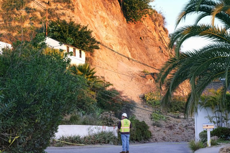 A city worker assesses a street where a landslide occurred in the Hollywood Hills area of Los Angeles on Jan. 31. The home's backyard crumbled, sending mud and debris down a slope, across a street and into the front yards of two other houses. (AP Photo/Richard Vogel)