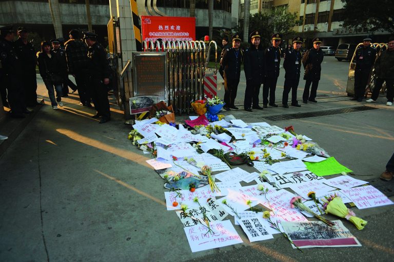 Security guards stand near protest banners and flowers are laid outside the headquarters of Southern Weekly newspaper in Guangzhou, Guangdong province Monday, Jan. 7, 2013. A dispute over censorship at the Chinese newspaper known for edgy reporting evolved Monday into a political challenge for China's new leadership as prominent scholars demanded a censor's dismissal and hundreds of protesters called for democratic reforms. (AP Photo)