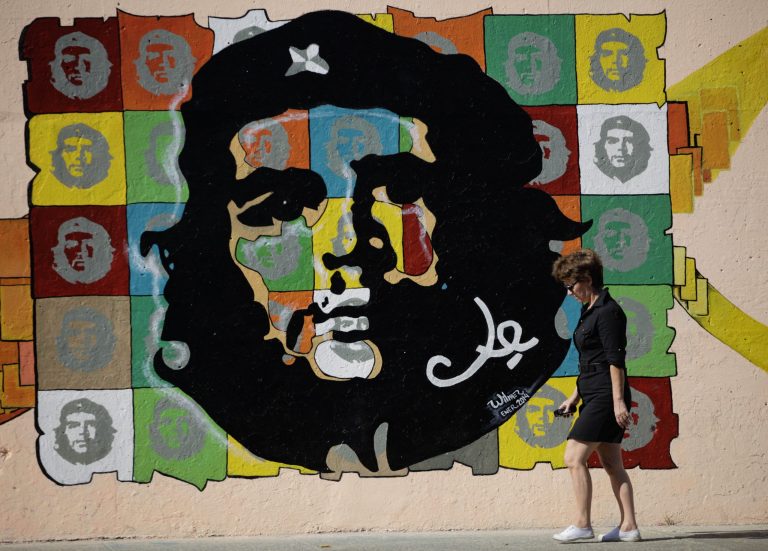 A woman walks in front of a mural depicting images of Ernesto 