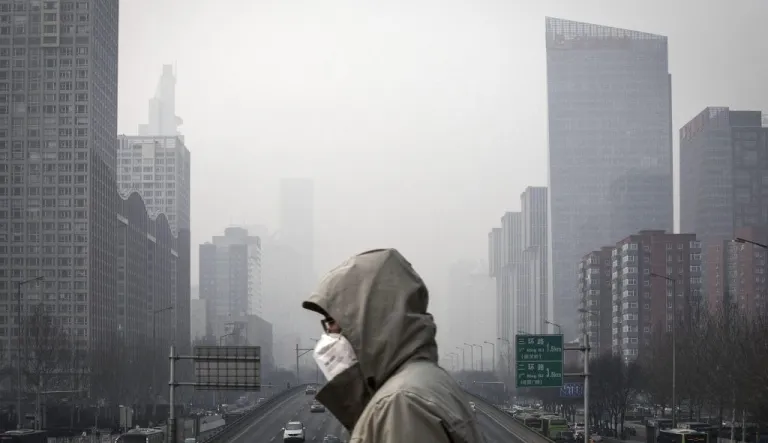 A man wearing a face mask in China walks on a footbridge as buildings are shrouded in haze.