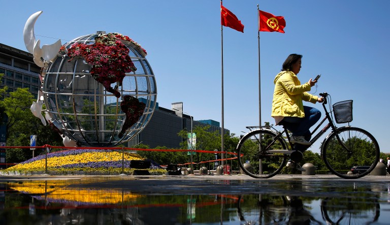 A woman rides a bicycle past a globe structure on display outside a bank in Beijing, Monday, May 6, 2019.