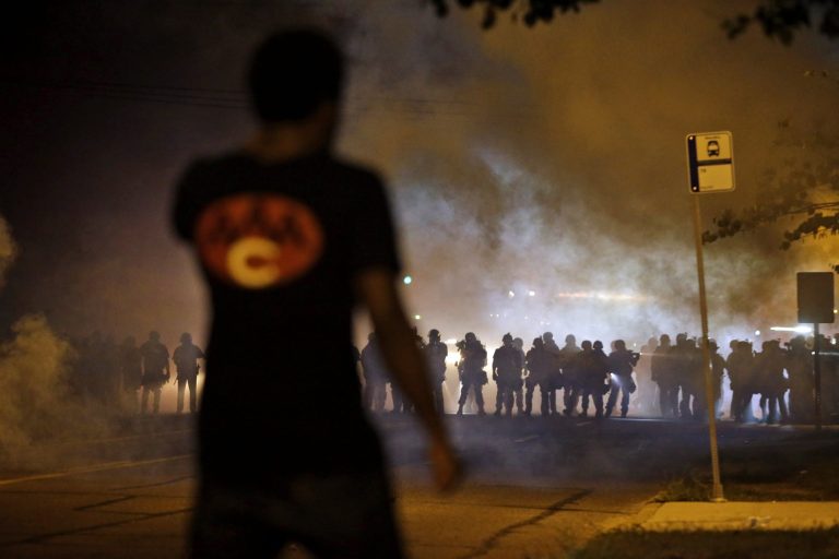 A man watches as police walk through a cloud of smoke during a clash with protesters Wednesday in Ferguson, Mo. (AP/Jeff Roberson)