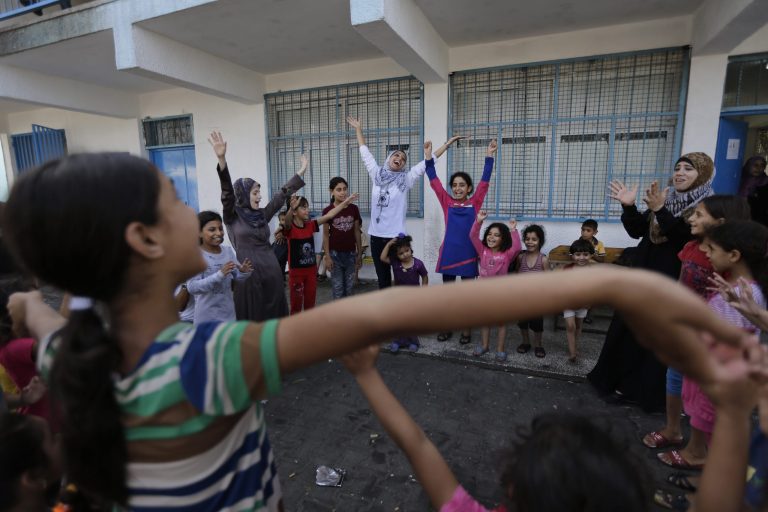 Volunteer Nisreen Shawa, 25, centre,  leads a play session with displaced Palestinian children at a U.N. school where they had sought refuge along with their families during the war, in Gaza City, Gaza Strip, Thursday, Aug. 7, 2014. Taking advantage of the continuing ceasefire, volunteers from the local non-profit NGO 'Tomooh' (Ambition), arranged a special play session for children to try and lessen the stress they've been enduring after the weeks of conflict. In the playground the children got a chance to sing and play group games under the caring eye of volunteers. They hope that their efforts will lessen the damage of the traumatic recent weeks events, or at least help them forget for a short while. (AP Photo/Lefteris Pitarakis)