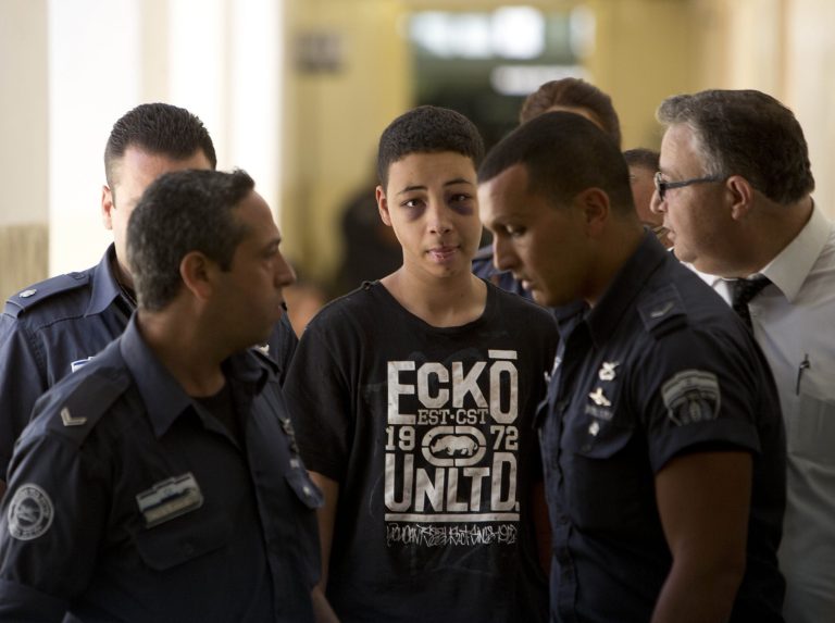Tariq Abu Khdeir, 15, a U.S. citizen who relatives say was beaten and arrested by Israeli police during clashes sparked by the killing Thursday of his cousin Mohammed Abu Khdeir, is escorted by Israeli prison guards during an appearance at Jerusalem magistrate's court Sunday, July 6, 2014. (AP Photo/Oded Balilty)