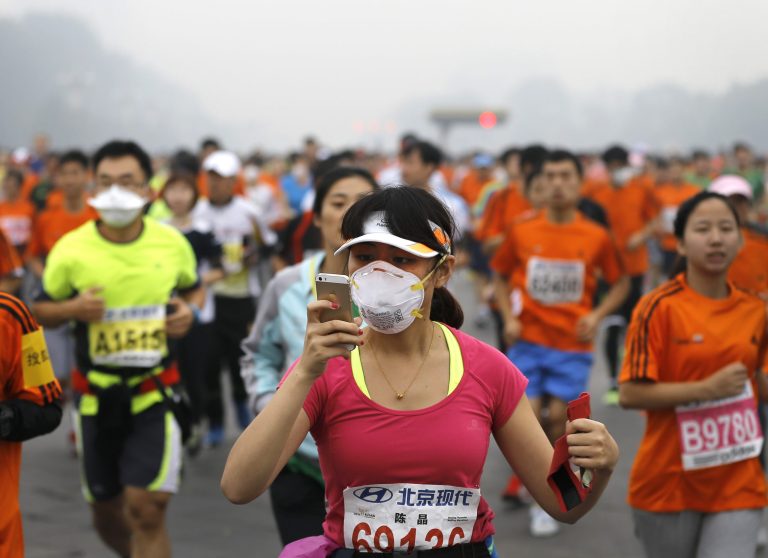 A runner, wearing a mask to protect herself from pollutants, looks at her smartphone as she and others jog past Chang'an Avenue near Tiananmen Square shrouded in haze at the start of 2014 Beijing International Marathon in Beijing, China Sunday, Oct. 19, 2014. (AP Photo/Andy Wong)
