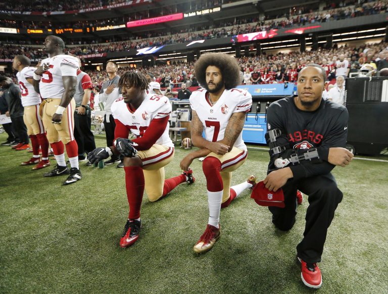 In this Dec. 18, 2016, file photo, San Francisco 49ers quarterback Colin Kaepernick (7) and outside linebacker Eli Harold (58) kneel during the playing of the national anthem before an NFL football game against the Atlanta Falcons in Atlanta. The blackballed quarterback was honored as Week 1 Community MVP by the players' union for his latest $100,000 donation and a back-to-school giveaway in New York City. (AP Photo/John Bazemore)