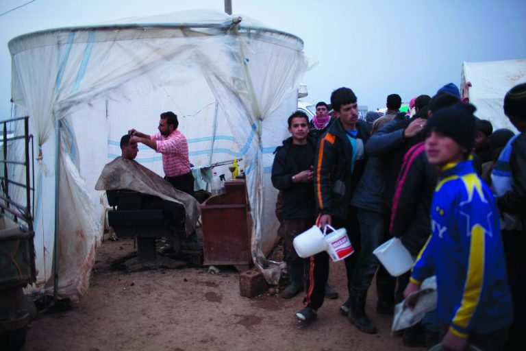 A displaced Syrian is seen within a makeshift barber shop while others stand in line for food in the Azaz camp for displaced people, north of Aleppo province, Syria, Friday, Feb. 22, 2013. According to Syrian activists the number of people in the Azaz camp has grown by 3,000 in the last weeks due to heavier shelling by government forces. (AP Photo/Manu Brabo)