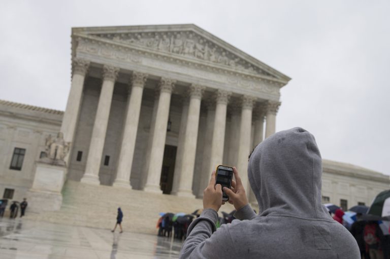 FILE - This April 29, 2014 file photo shows a visitor to the Supreme Court uses his cellphone to take a photo of the court in Washington. A divided Supreme Court sided with gun control groups and the Obama administration Monday, ruling that the federal ban on 