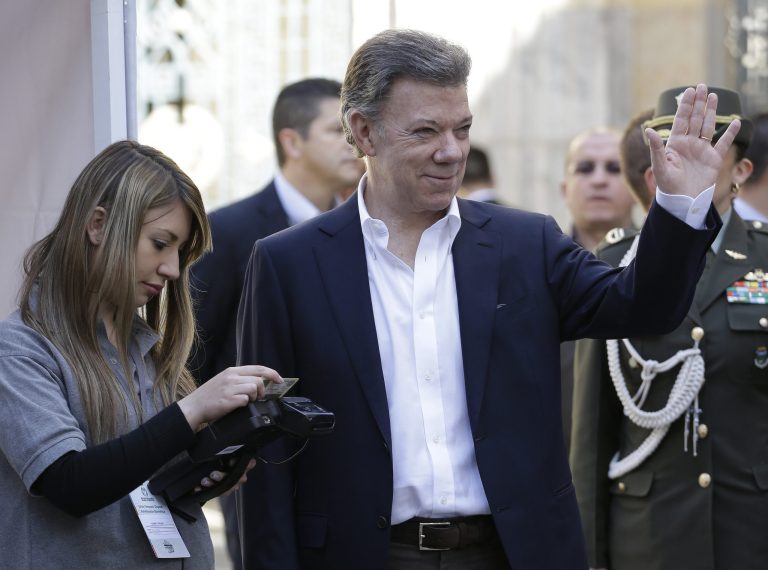 President Juan Manuel Santos waves to reporters a an electoral official checks his before voting in presidential elections in Bogota, Colombia, Sunday, May 25, 2014. Santos is seeking a second four-year term as candidate for the Social Party of National Unity. (AP Photo/Fernando Vergara)