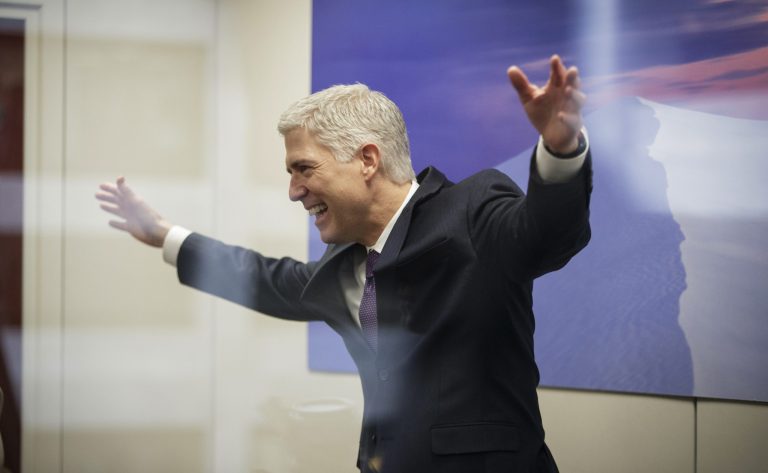 Supreme Court Justice nominee Neil Gorsuch, seen through glass, makes an animated gesture while speaking with staff members during his confirmation period. He's not a household word yet. (AP Photo/J. Scott Applewhite)