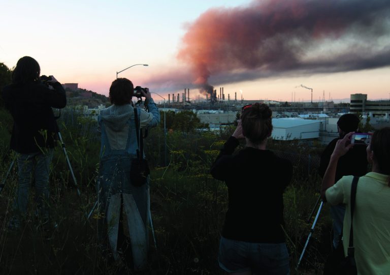 The curious gather on a hillside in Point Richmond, Calif., to photograph the the fire in an oil unit at the Chevron refinery in Richmond, Calif., Monday, Aug. 6, 2012. Officials have told residents of two Northern California cities to shelter-in-place as a fire at a Chevron refinery in Richmond releases plumes of black smoke. (AP Photo/D. Ross Cameron/) (AP Photo/The Contra Costa Times, D. Ross Cameron) NO SALES MAGS OUT LOCALS PLEASE CREDIT
