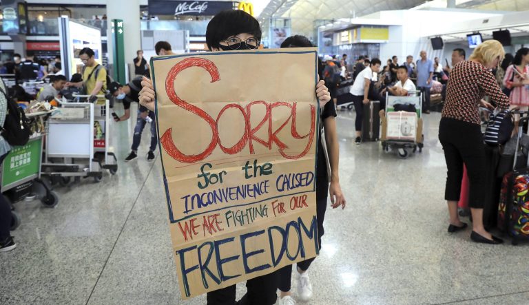 A protester shows a placard to stranded travelers during a demonstration at the Airport in Hong Kong, Tuesday, Aug. 13, 2019.