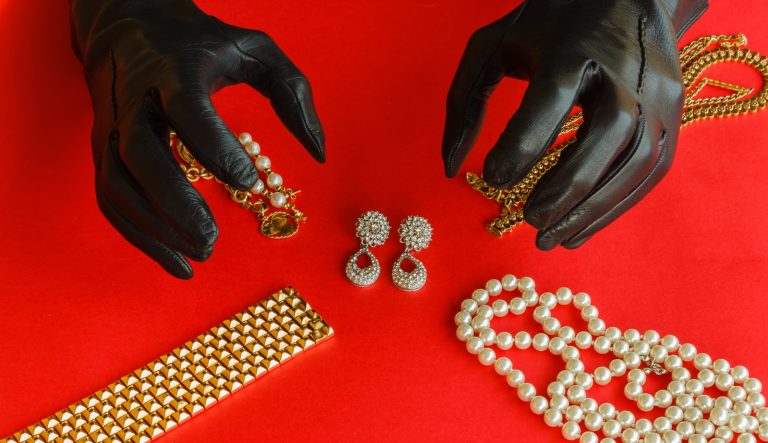 two hands wrapped in black gloves are going to steal a set of necklaces,bracelets and earrings of gold and diamonds 