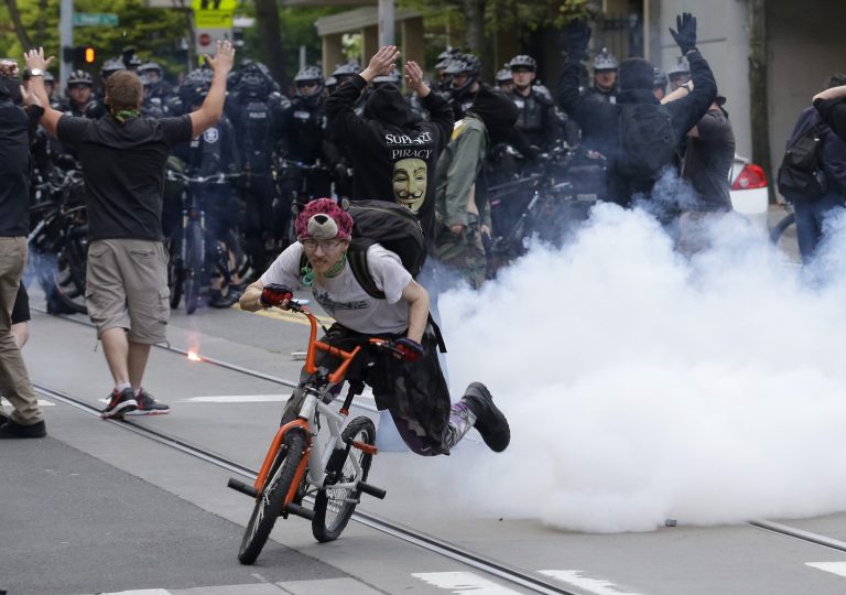 A man rides his bike away after a police flash-bang device exploded in a crowd of protesters taking part in a May Day anti-capitalism march, Friday, May 1, 2015 in Seattle. (AP Photo/Ted S. Warren)