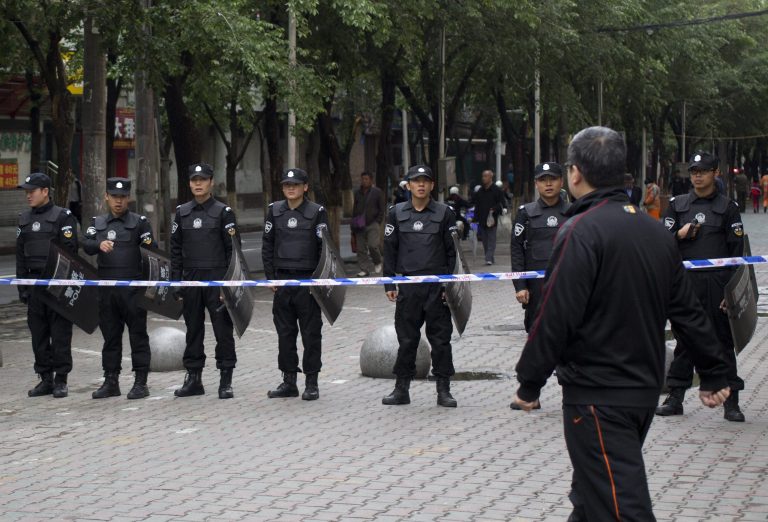 A man walk past policemen standing guard near a road leading to the site of  Thursday's explosion in Urumqi, China's northwestern region of Xinjiang, Friday, May 23, 2014. Authorities closed the street market after attackers hurled bombs from two SUVs that plowed through shoppers on Thursday, killing dozens and wounding more than 90. (AP Photo/Andy Wong)