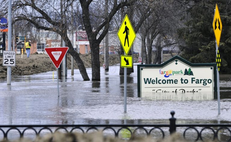 FILE - In this April 8, 2011 file photo, a welcome sign for Fargo, N.D., sits in the rising floodwaters of the Red River as a flood engineer for the U.S. Army Corps of Engineers, at left, inspects the levee protecting the downtown area. The Red River Diversion Authority is meeting Thursday, March 13, 2014, in Fargo for the first time since President Obama left the project out of his budget plans. The $2 billion channel would move water around Fargo and neighboring Moorhead, Minn., which has prepared for major floods in four of the last five years. (AP Photo/Jim Mone, File)