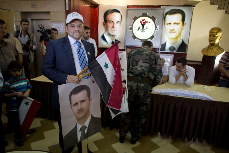 A man holds a portrait of President Bashar Assad and a national flag at a polling station in Damascus, Syria, Tuesday, June 3, 2014. Polls opened in government-held areas in Syria amid very tight security Tuesday for the country's presidential election, a vote that President Bashar Assad is widely expected to win. (AP Photo/Dusan Vranic)