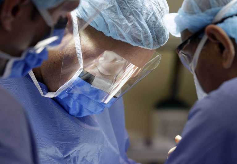 In this Aug. 6, 2014 photo, Dr. Jared Bernard, a lieutenant commander and trauma surgeon in the U.S. Navy, helps perform surgery on a gunshot victim alongside medical personnel at Cook County's Stroger Hospital in Chicago. A program launched in late spring has Navy doctors, nurses and medics training at the hospital because patients arriving there often have the same types of wounds that are common in combat. (AP Photo/Nam Y. Huh)