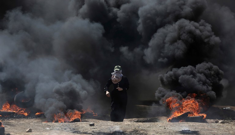 A Palestinian woman walks through black smoke from burning tires during a protest on the Gaza Strip's border with Israel, Monday, May 14, 2018. The Islamic militant group Hamas that rules Gaza, and is leading the rallies, says protests will continue until a blockade, in place since it took over Gaza in 2007, is broken.