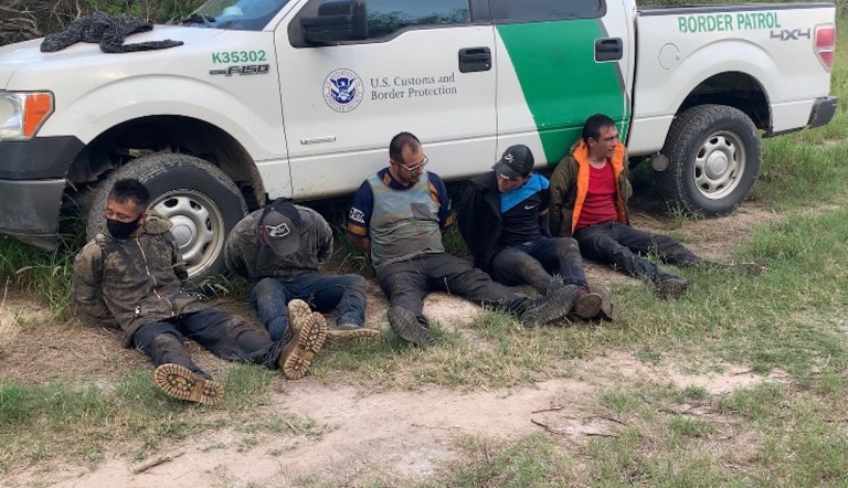 Five men are taken into custody by agents. Two men, seated on the left, are suspected by Border Patrol Agent Christian Alvarez to be smugglers who were leading the other three through the brush.
