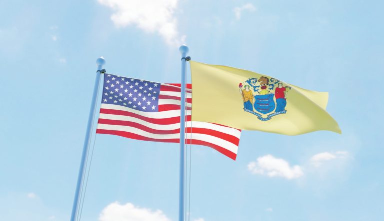 USA and New Jersey state flags waving against blue sky.