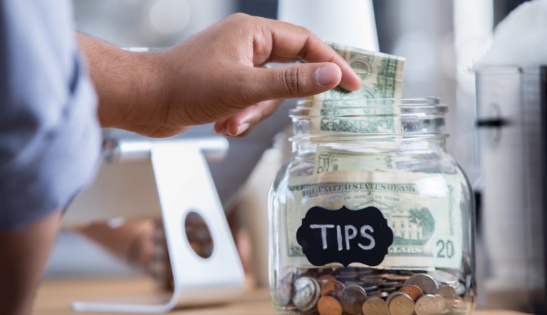 Customer places cash into a tip jar.