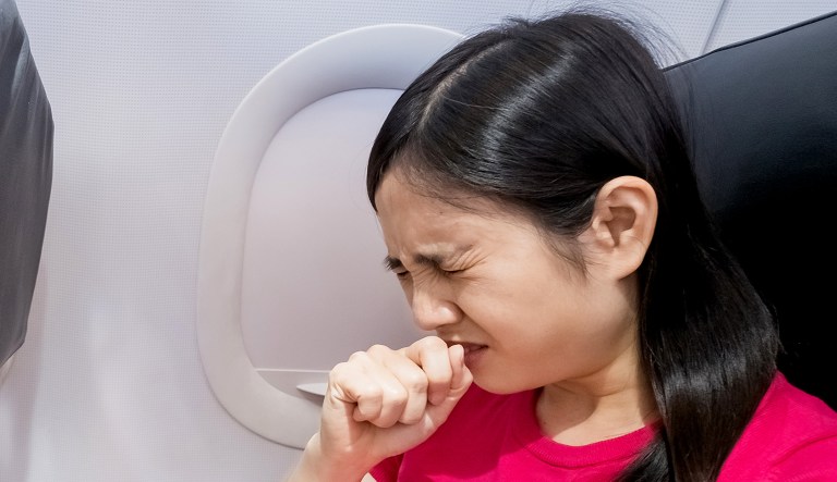 A sick person is seen in an airplane with her hand over her mouth, as if sneezing or coughing.