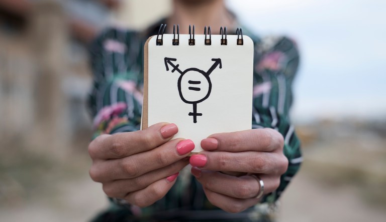 Closeup of a young woman outdoors showing a notepad in front of her with a transgender symbol drawn in it. 
