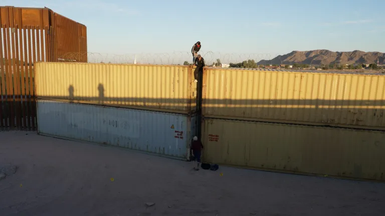 Three migrants from Cuba, climb over shipping containers used as a make shift border wall to illegally cross the border into the United States.