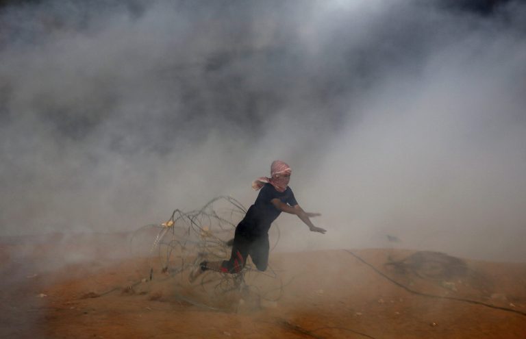 A Palestinian protester falls down on a barbed fence as he runs for cover from teargas fired by Israeli troops during a protest east of Khan Younis on Friday. The Israeli military said about 20,000 protesters participated.