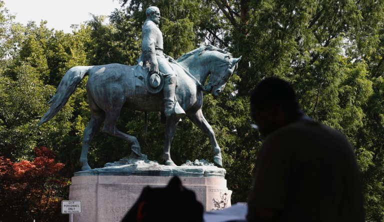 In this Monday, Aug. 6, 2018, photo, a visitor eats lunch in front of a statue of Robert E. Lee that is surrounded by fencing and a No Trespassing sign in Charlottesville, Va., at the park that was the focus of the Unite the Right rally. 
