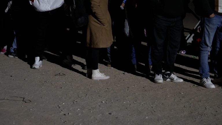 People standing in line waiting to be processed by border patrol are asked to remove their shoelaces