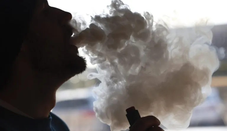 A person smokes using a vape cartridge and exhales a cloud of smoke.